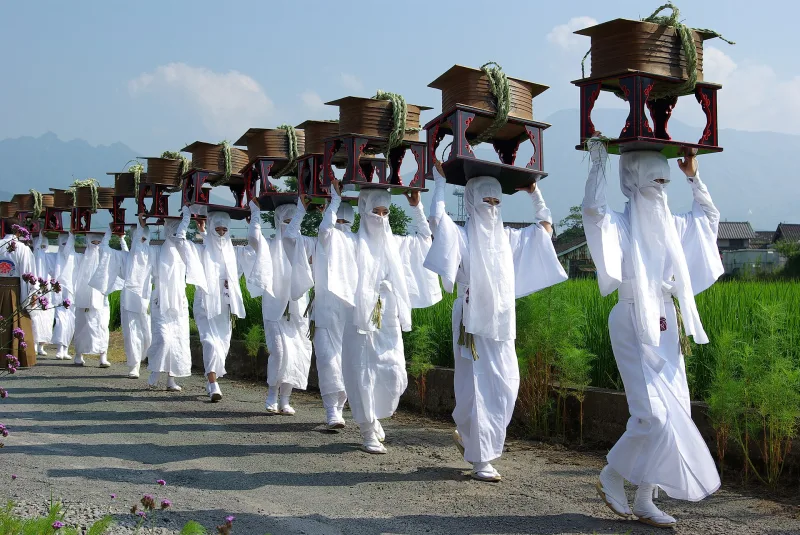 Women in white robes carrying offerings on their heads in the Onda Festival procession at Aso Shrine