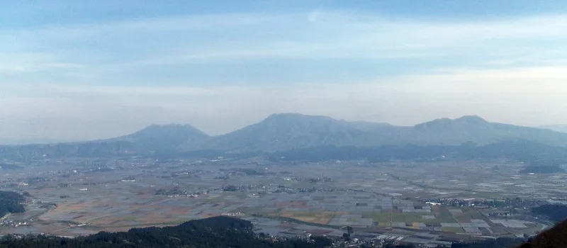 The five peaks of Mt. Aso rising beyond the farmland of the Aso Valley, seen from Daikanbo