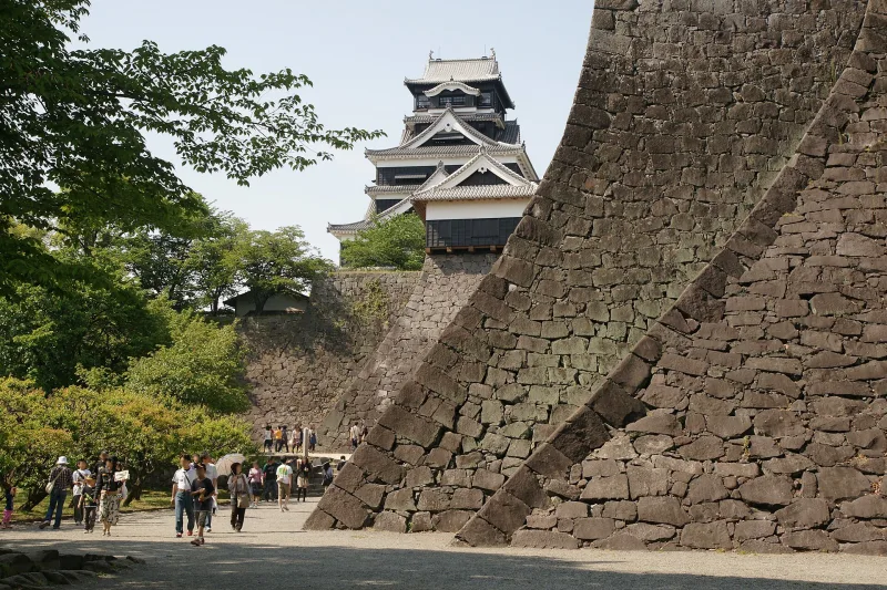 Steeply curving stone walls of Kumamoto Castle with the keep rising behind