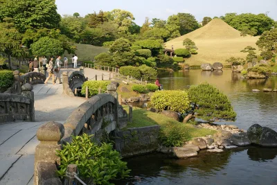 Stone bridge over the spring-fed pond with the Fuji-shaped mound behind at Suizenji Jojuen