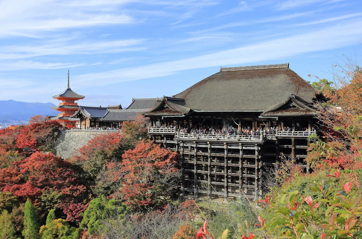 Kiyomizu-dera's main hall and wooden stage rising above red autumn maples, with a pagoda behind