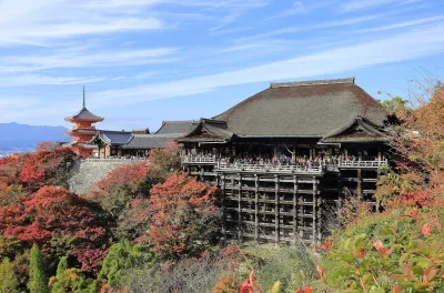Kiyomizu-dera's main hall and wooden stage rising above red autumn maples, with a pagoda behind
