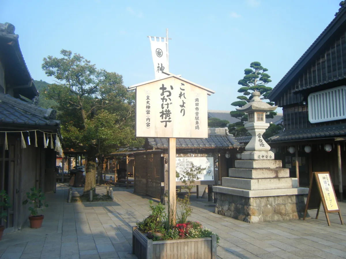 Entrance to Okage Yokocho with a wooden signpost and a large stone lantern among old-style buildings