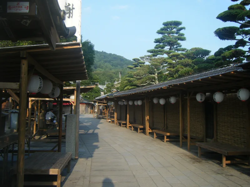 A stone-paved lane of Okage Yokocho lined with wooden stalls and paper lanterns