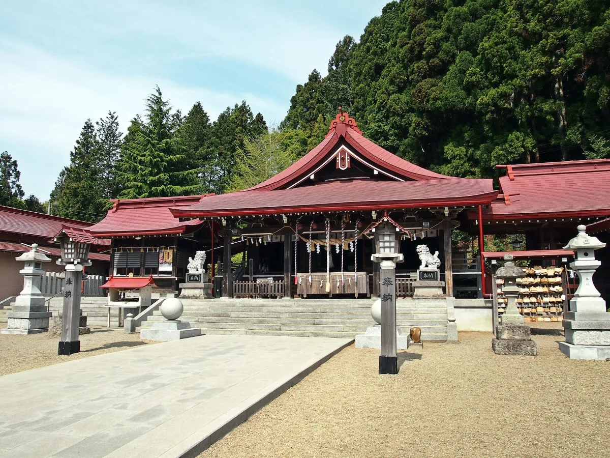 Red-roofed worship hall of Kanahebisui Shrine in front of a wooded hillside