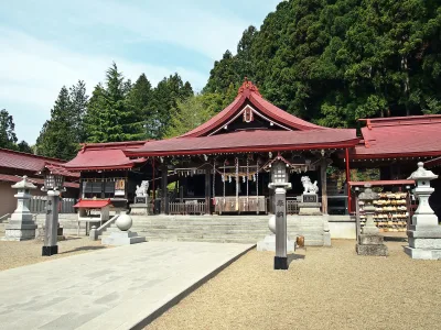 Red-roofed worship hall of Kanahebisui Shrine in front of a wooded hillside
