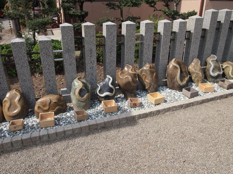 Row of dark snake-patterned jamon stones along a gravel path at Kanahebisui Shrine