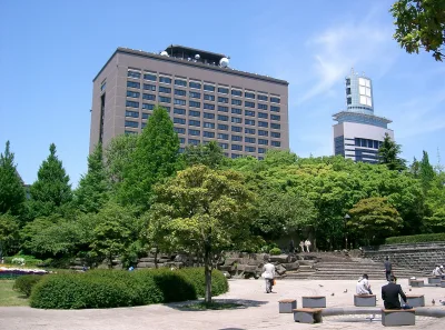 Green trees and paved plaza of Kotodai Park with the Miyagi Prefectural Office tower behind
