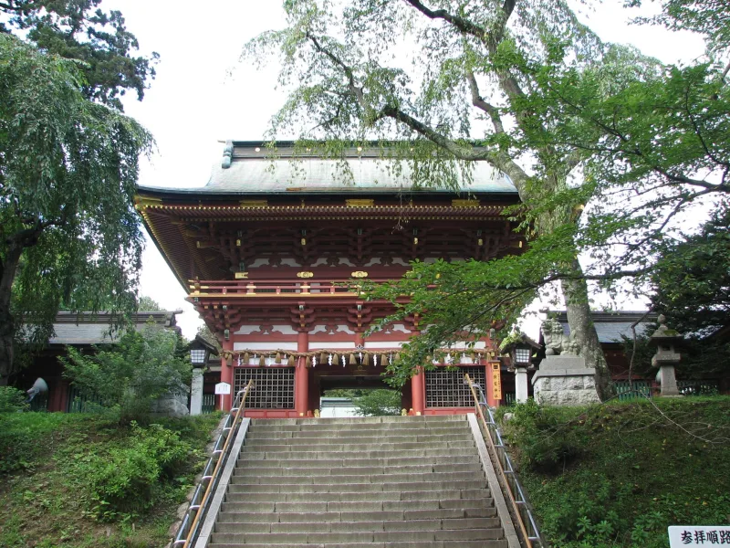 Red two-story gate of Shiogama Shrine at the top of a long stone stairway