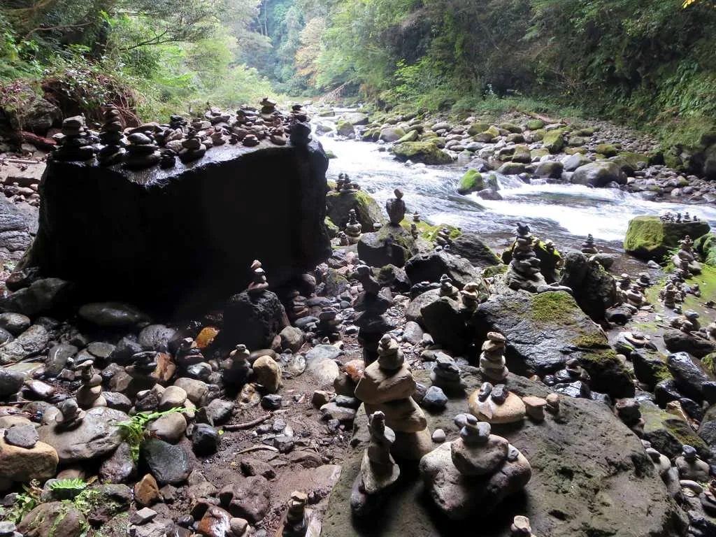 The sacred rock cave at Amanoyasugawara, with visitors’ stone piles beneath the rocky overhang.