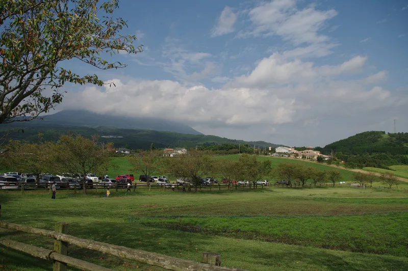 Lawns and farm buildings of Takachiho Farm with the Kirishima mountains in the clouds behind