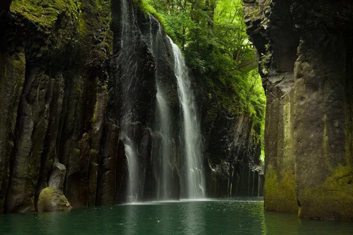 Manai Falls pouring into the green river between basalt column cliffs at Takachiho Gorge