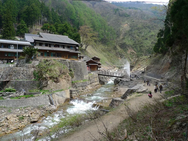 Wooden inn buildings, a steaming geyser and a river in the Jigokudani valley
