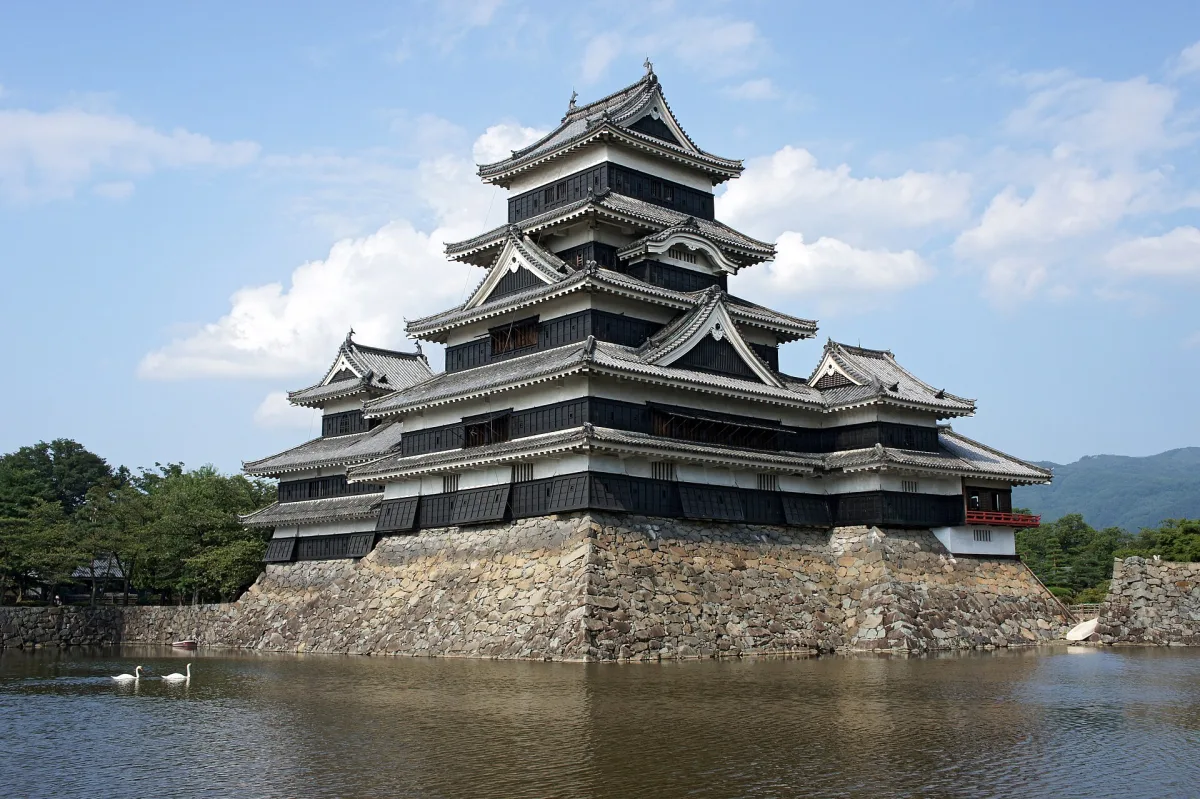 The black five-tiered keep of Matsumoto Castle reflected in its moat under a blue sky