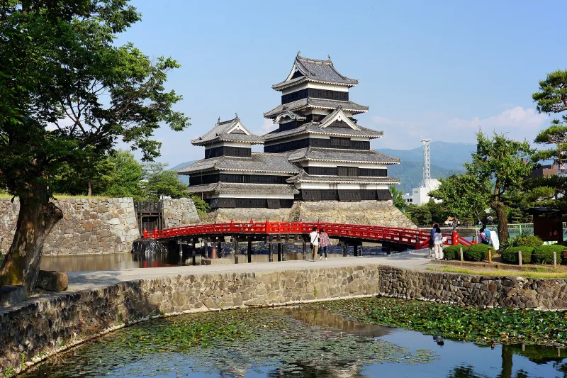 Matsumoto Castle keep seen across the moat with a red wooden bridge and trees