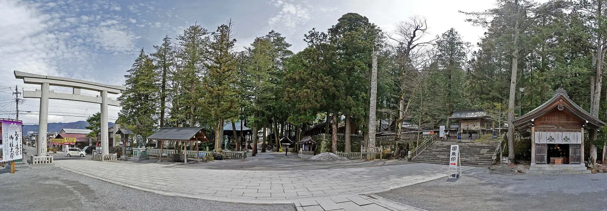 Wide view of the Suwa Taisha Kamisha Honmiya grounds with a stone torii and tall cedars