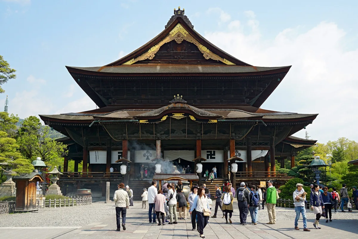 The large main hall of Zenko-ji with its sweeping roof, visitors in the stone-paved courtyard