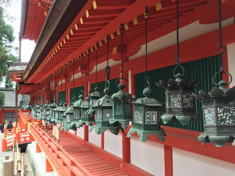 Row of bronze hanging lanterns along a vermilion corridor at Kasuga Taisha
