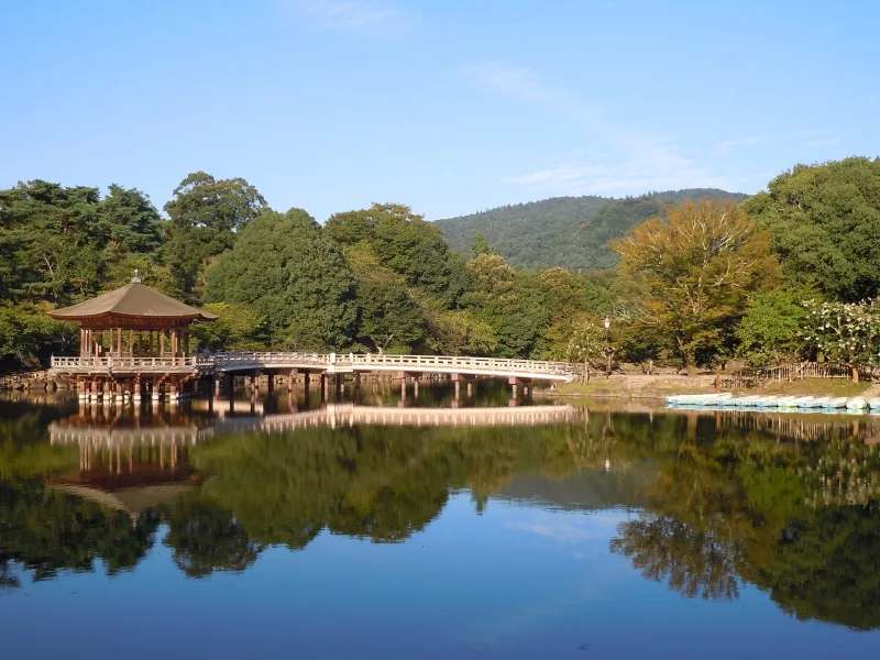 Ukimido pavilion and its bridge reflected in a calm pond, with wooded hills behind