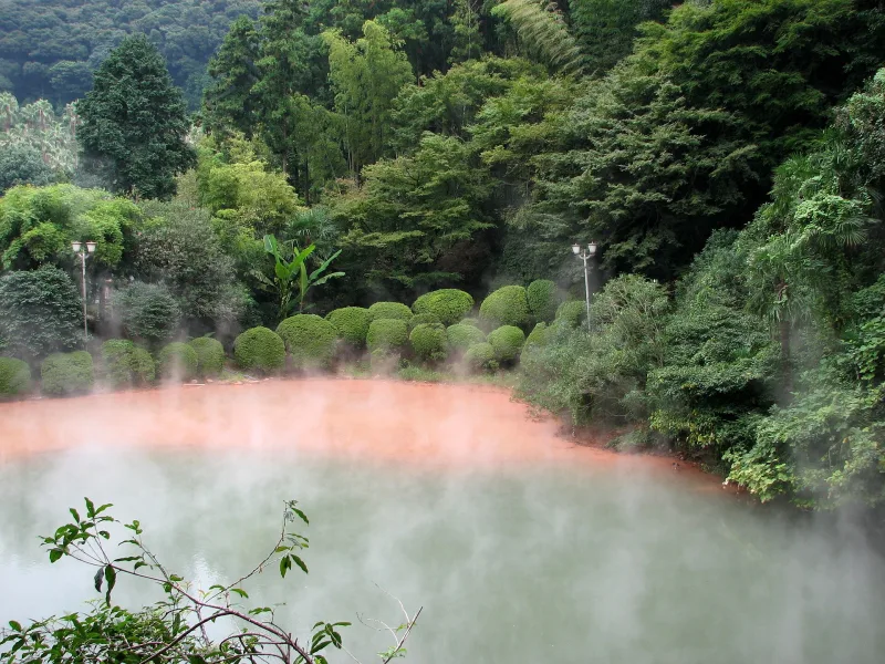Red water of Chinoike Jigoku edged by trimmed shrubs and forest