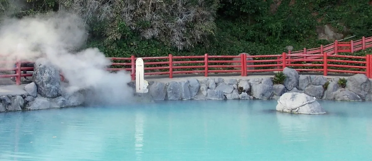 Steam rising over a milky blue hot spring pool with a red railing at Kamado Jigoku, Beppu