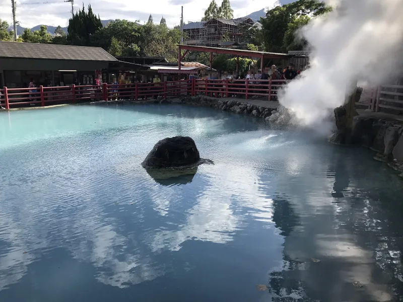 Pale blue pool with a dark rock and billowing steam at Kamado Jigoku