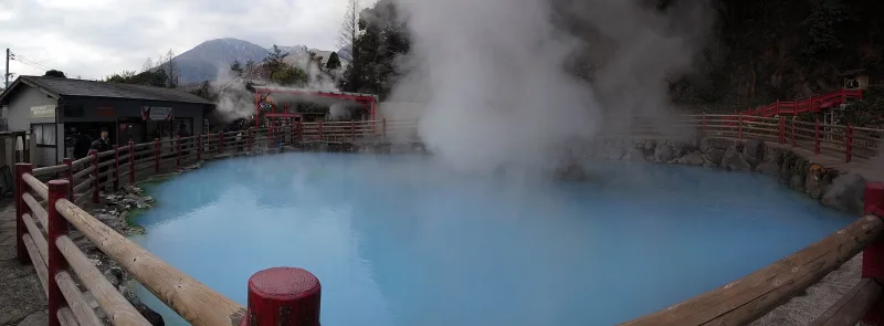 Hot spring pool enclosed by a wooden fence with a thick plume of steam at Kamado Jigoku