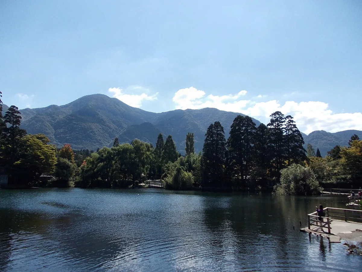 Lake Kinrin with a wooden deck, forest and mountains under a blue sky in Yufuin