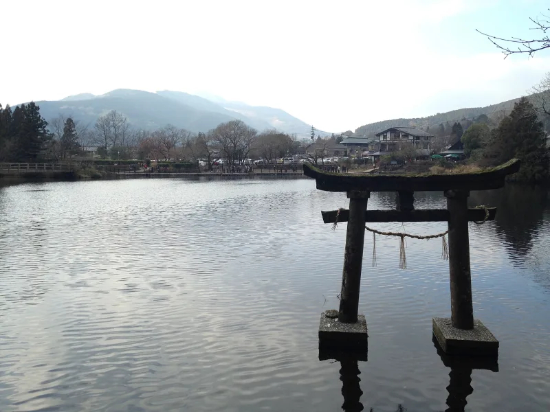 Stone shrine gate standing in the water of Lake Kinrin with mountains behind