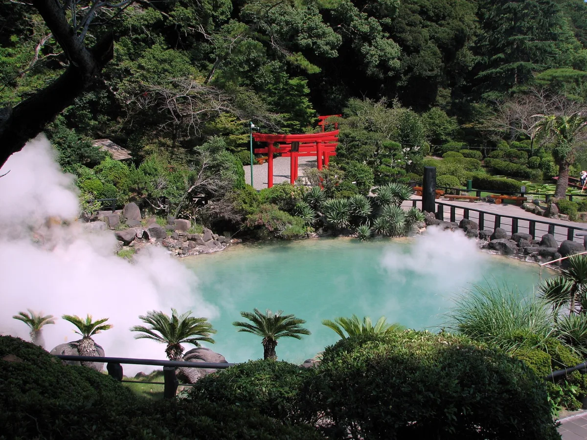 Cobalt-blue hot spring pool at Umi Jigoku, Beppu, with steam, palms and a red torii gate