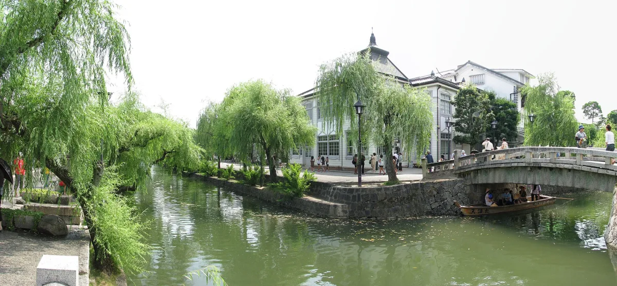 Willow-lined Kurashiki River with a stone bridge, a small boat and historic buildings in the Bikan Quarter