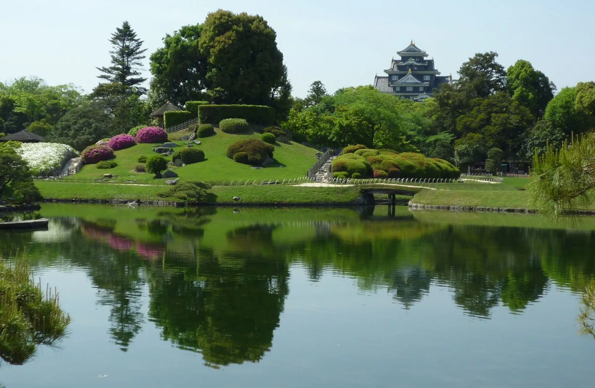 Pond in Okayama Korakuen Garden reflecting green hills, with the black keep of Okayama Castle behind