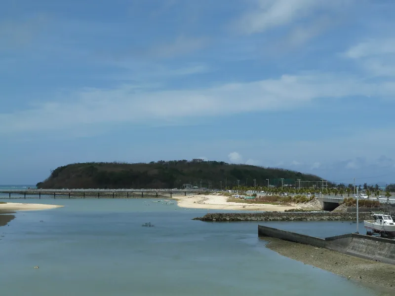The low green hill of Senaga Island seen across calm shallow water