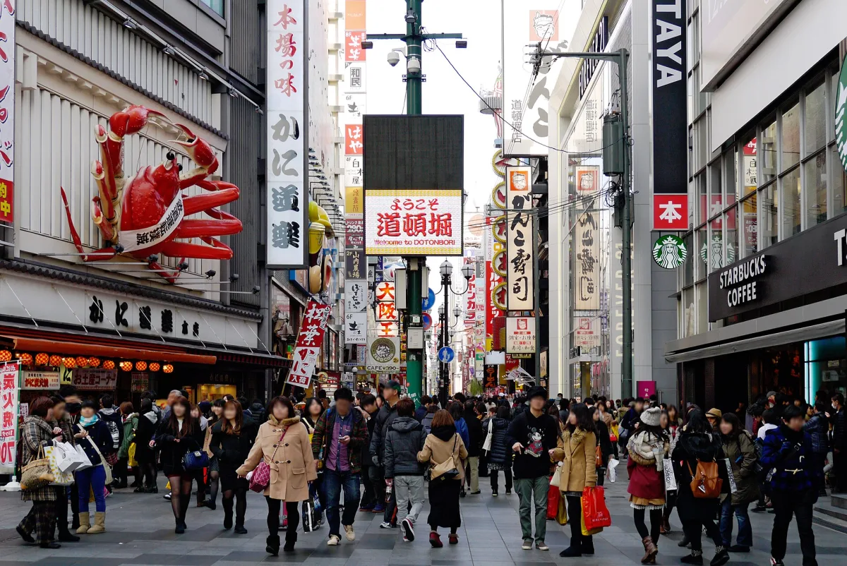 Crowded Dotonbori street lined with giant signs, including a huge mechanical crab