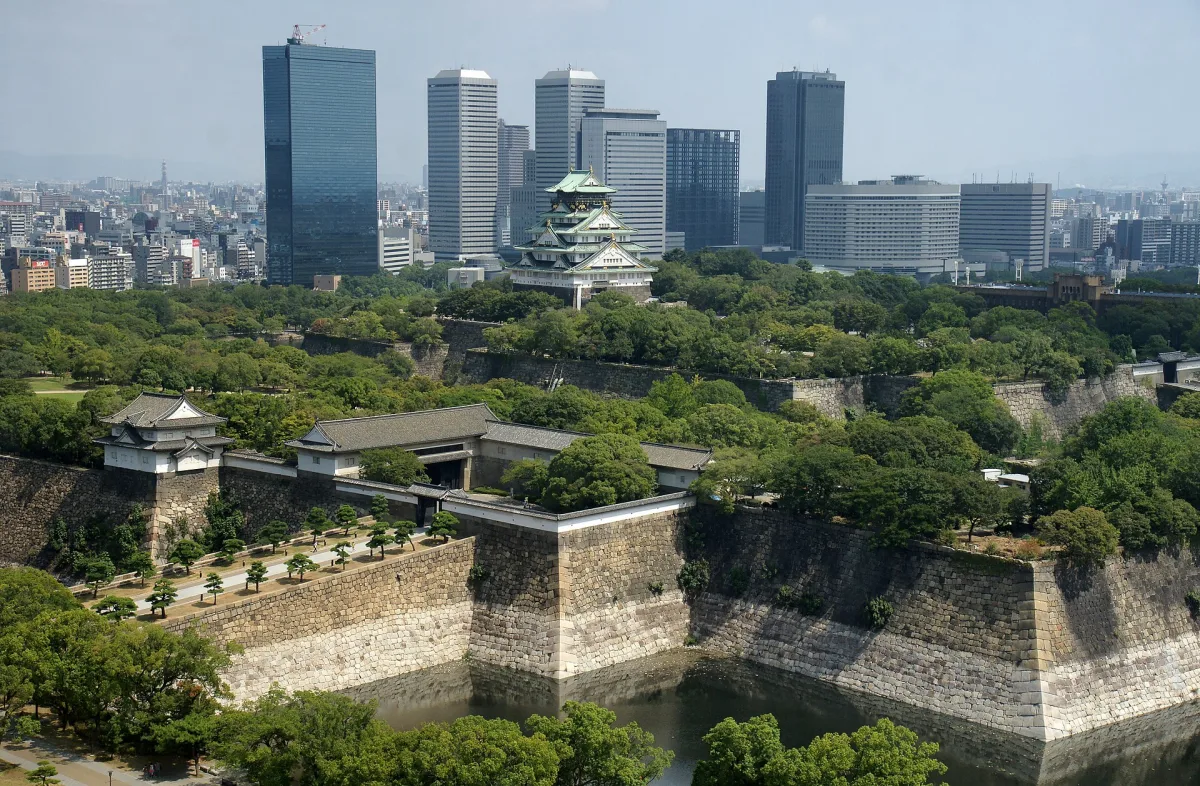 Osaka Castle keep rising above stone walls and moats, with the city's skyscrapers behind