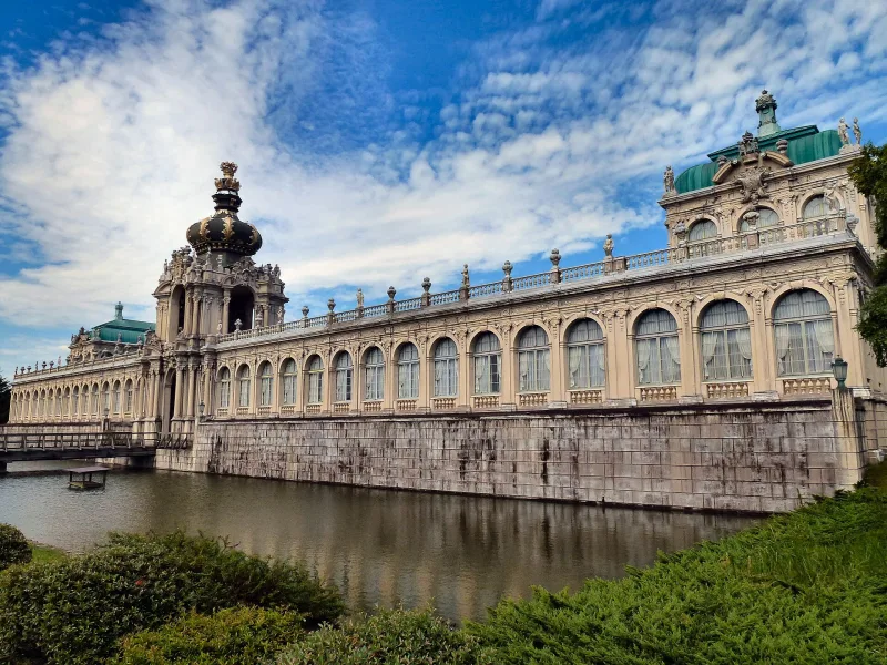 The long baroque facade of the Zwinger Palace replica reflected in a moat in Arita