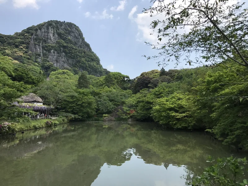 Garden pond reflecting green trees and the rocky peak of Mt. Mifune
