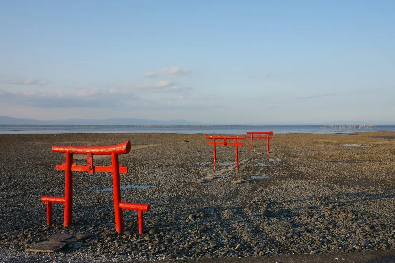 Row of red torii gates on the exposed sea bed of the Ariake Sea at low tide
