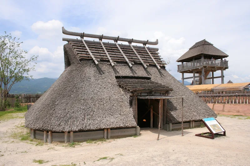 Reconstructed thatched pit dwelling with a wooden watchtower behind it