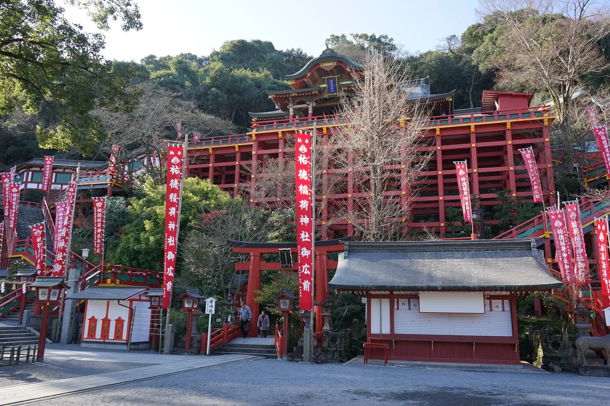 Yutoku Inari Shrine's vermilion main hall raised on a tall wooden stage against a wooded hillside