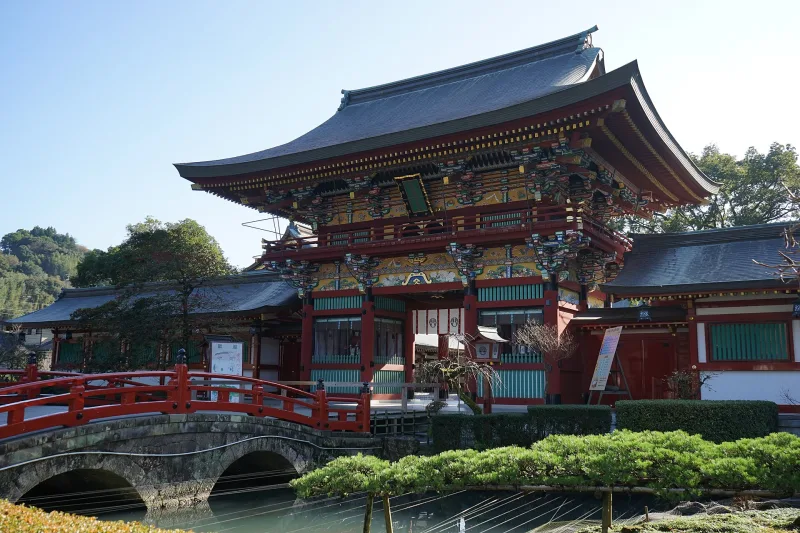 The ornate two-story vermilion gate of Yutoku Inari Shrine behind a stone bridge