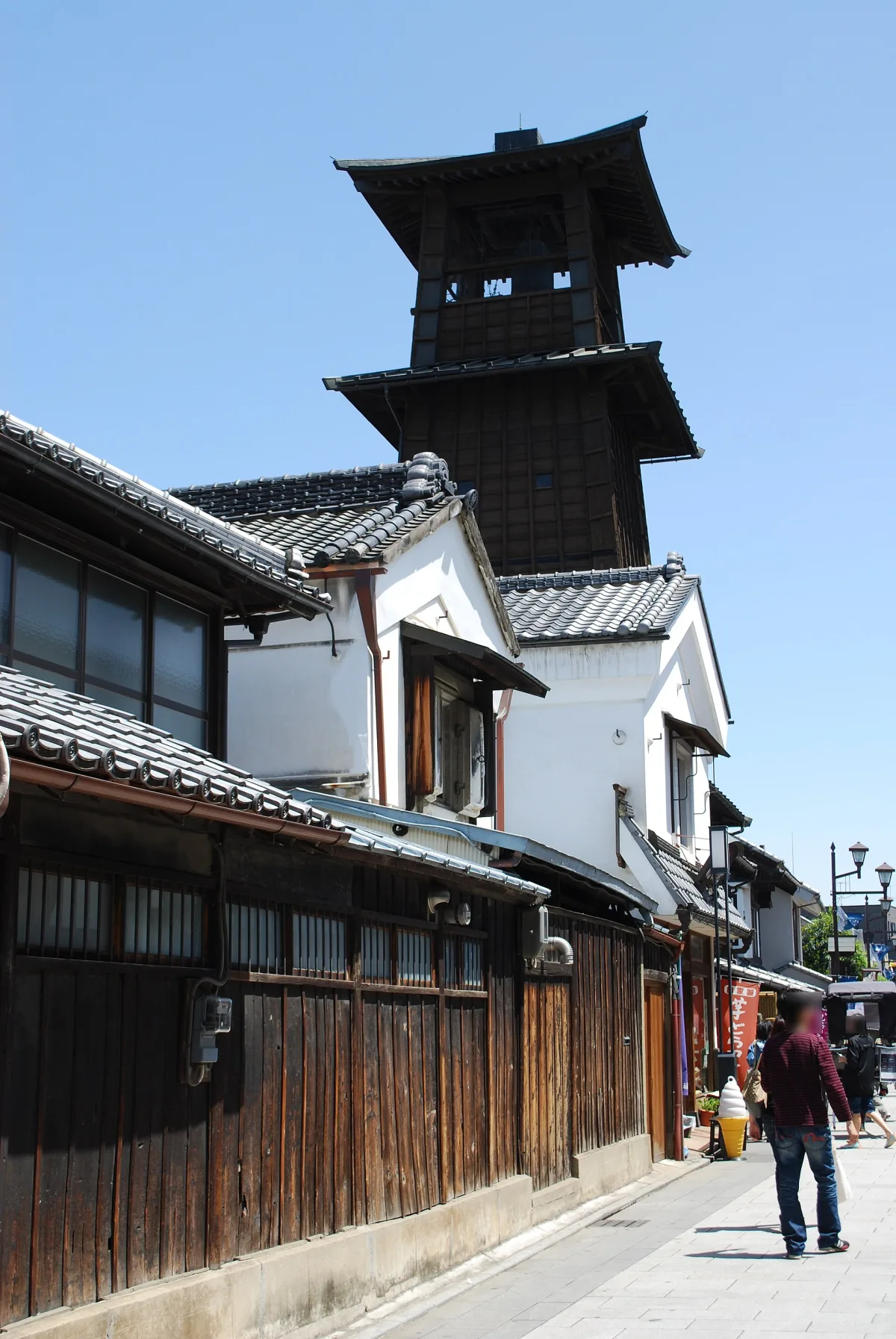 The dark wooden three-tiered Toki no Kane bell tower rising above old storehouse shops in Kawagoe
