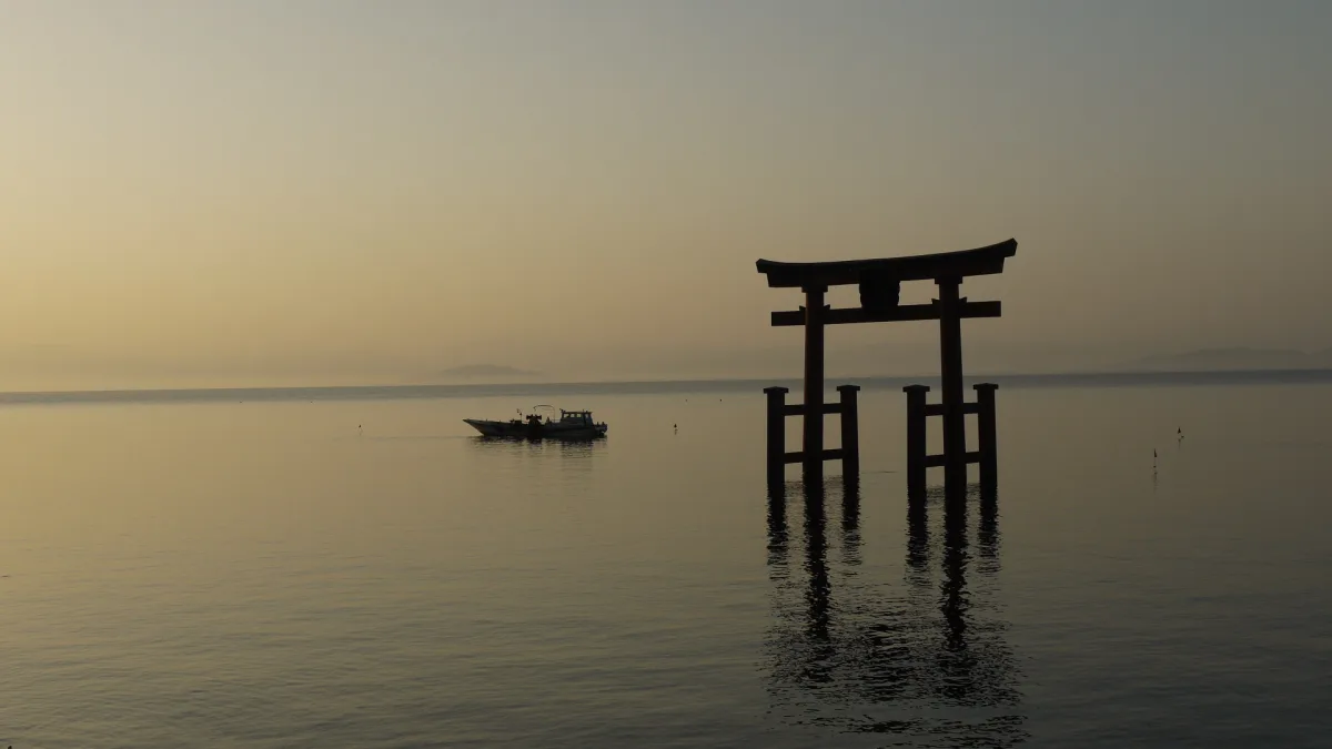 Shirahige Shrine's torii gate standing in Lake Biwa at dusk, with a small fishing boat
