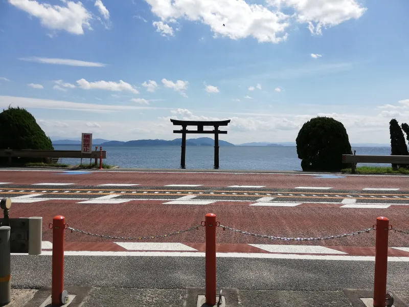Red torii gate in Lake Biwa seen across the road from Shirahige Shrine on a sunny day