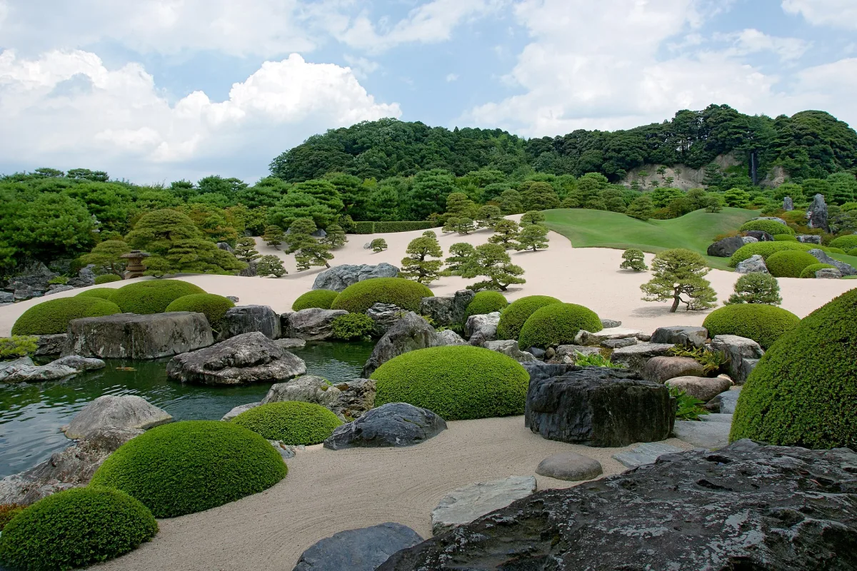 Dry landscape garden of the Adachi Museum of Art with white gravel, rounded shrubs and wooded hills behind