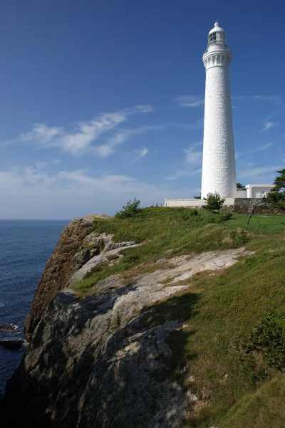 The white stone Hinomisaki Lighthouse standing on a grassy clifftop above the Sea of Japan