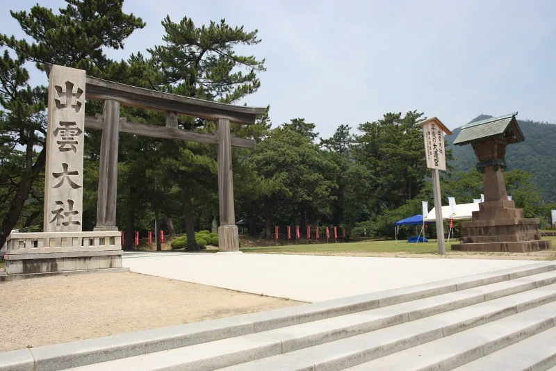 Wooden torii gate and stone marker carved with the name Izumo Taisha, framed by pine trees