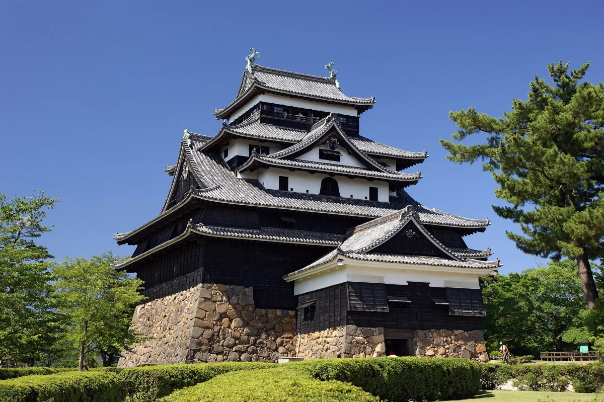 Black wooden keep of Matsue Castle on a stone base under a clear blue sky