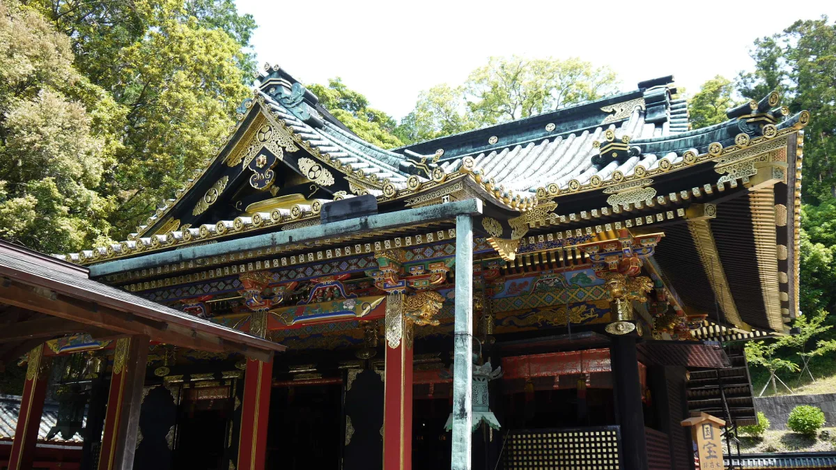 Ornate lacquered main hall of Kunozan Toshogu with gold and black carvings among green trees