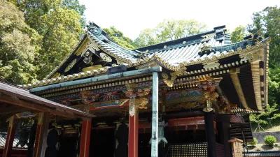 Ornate lacquered main hall of Kunozan Toshogu with gold and black carvings among green trees